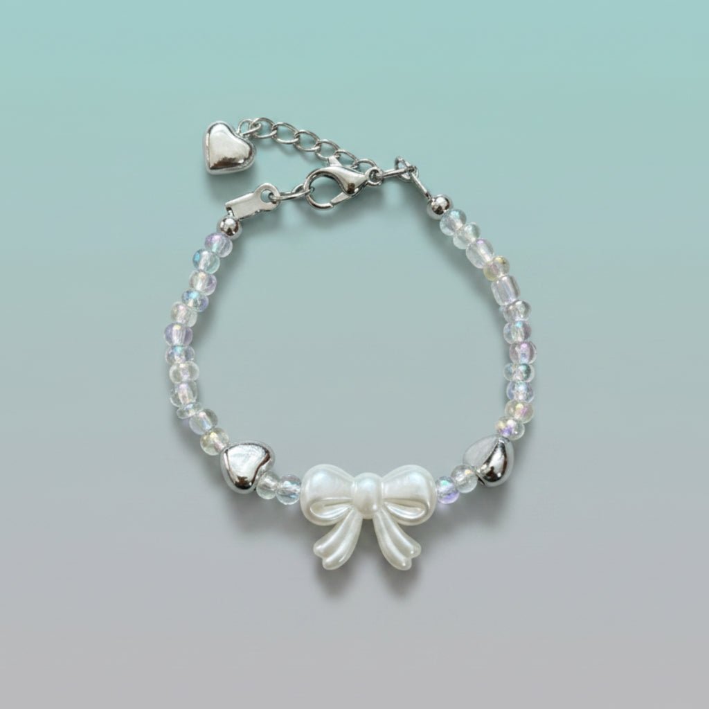Silver-toned bracelet with iridescent beads, a central white bow charm, and an adjustable chain featuring two small silver hearts.