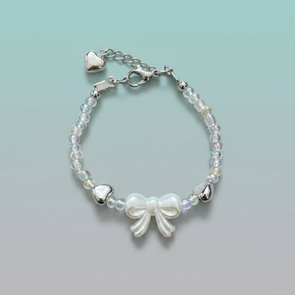 Silver-toned bracelet with iridescent beads, a central white bow charm, and an adjustable chain featuring two small silver hearts.