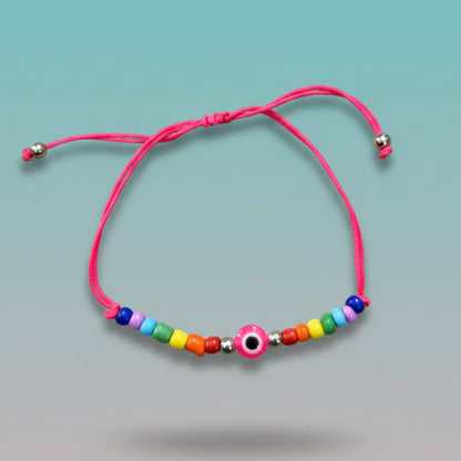 An adjustable pink string bracelet featuring a central pink and white evil eye charm, accented by small silver beads and a vibrant sequence of multi-colored beads on a light teal background.