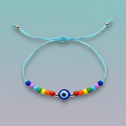 An adjustable light blue string bracelet featuring a central dark blue and white evil eye charm, accented by small silver beads and a vibrant sequence of multi-colored beads on a light teal background.