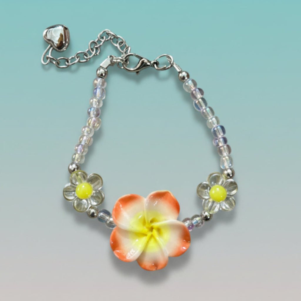 Nature-inspired beaded bracelet featuring a prominent orange and yellow plumeria flower charm, clear iridescent beads, and a small silver heart pendant on a light teal background