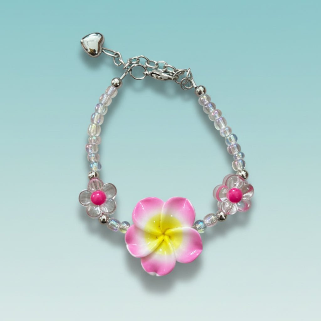 Beaded chain bracelet featuring a prominent pink and yellow tropical plumeria flower charm, clear iridescent beads, two small pink flower accents, and a silver heart charm on a light teal background.