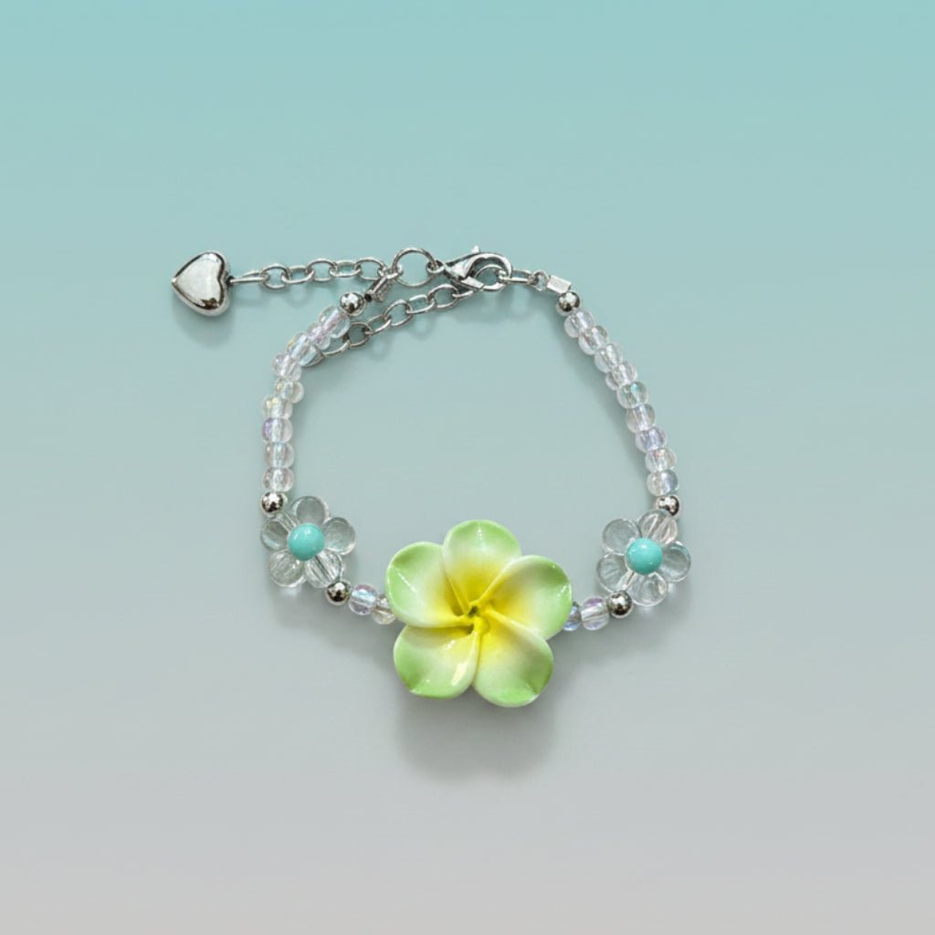 Nature-inspired beaded bracelet featuring a prominent lime green and yellow plumeria flower centerpiece, clear iridescent beads, two small turquoise flower accents, and a silver heart charm on a light teal background.