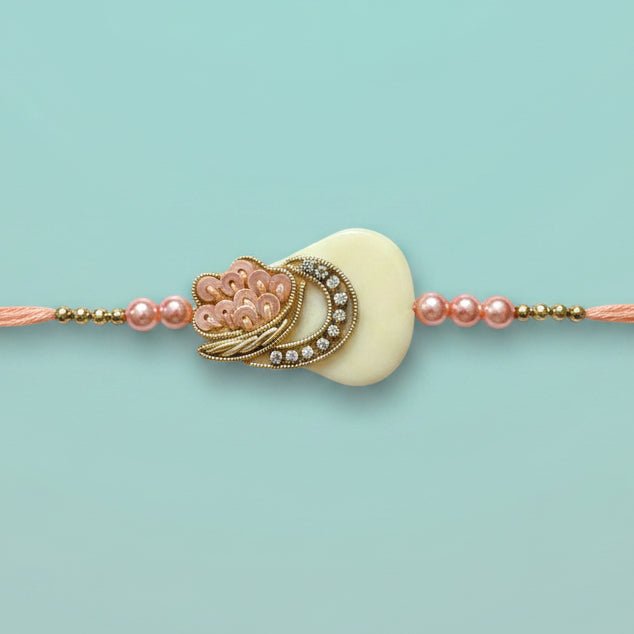 Gifthubmart Peach Tara Rakhi with peach thread and ornate cream pendant with gold-tone accents.