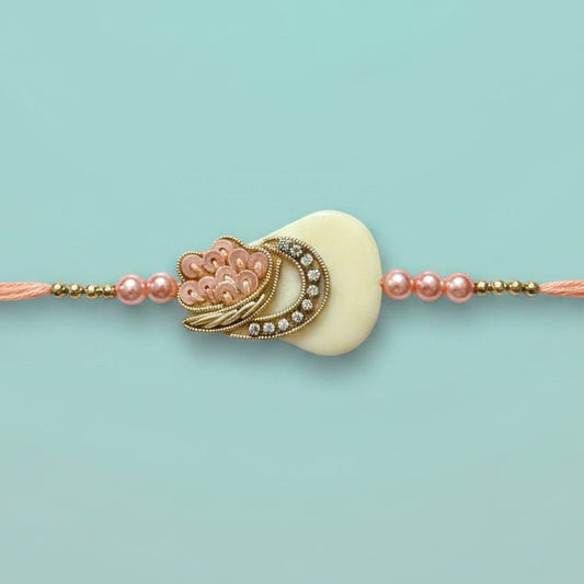 Gifthubmart Peach Tara Rakhi with peach thread and ornate cream pendant with gold-tone accents.