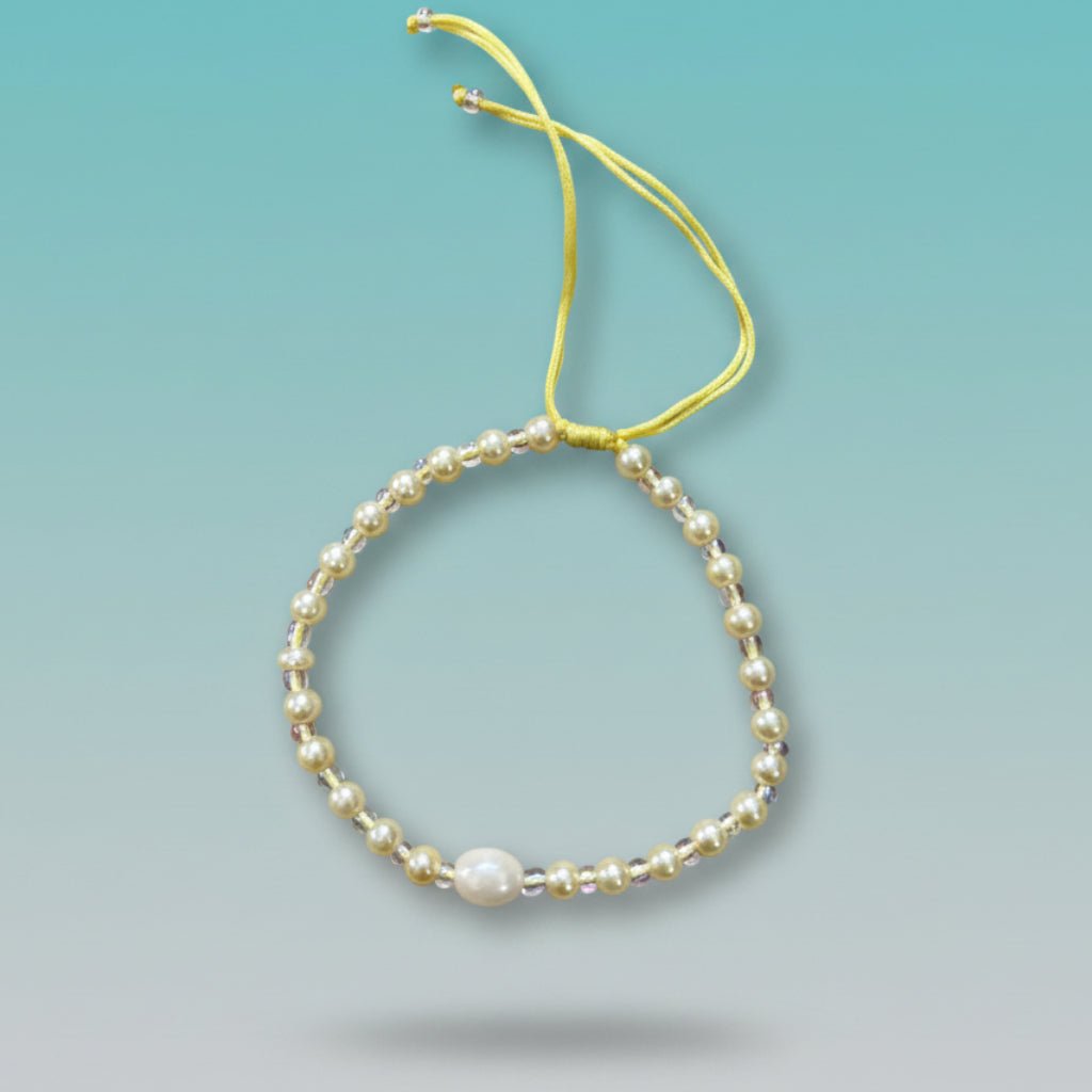 Handmade adjustable yellow string bracelet featuring a large central white pearl, accented by small alternating gold and clear beads on a soft mint green background.