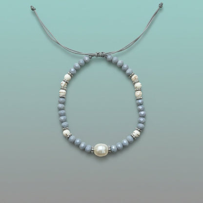 Delicate handmade adjustable string bracelet featuring a large central white pearl, accented by smaller light blue and marbled white beads with silver spacers on a soft mint green background.