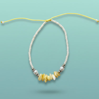 Delicate seashell bracelet featuring white beads and warm yellow stone accents on a light blue background.