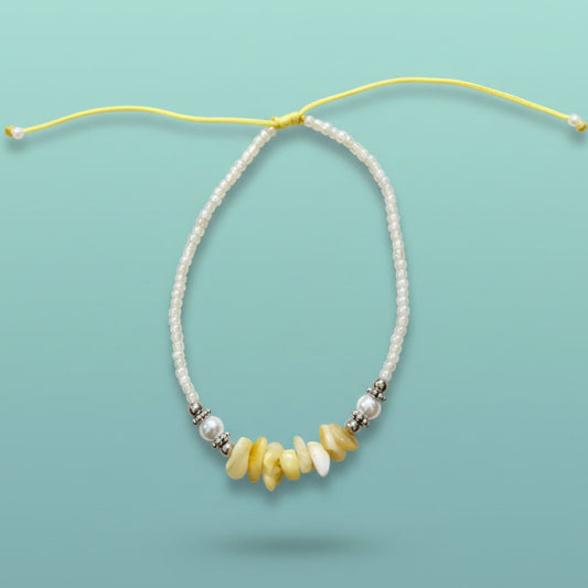 Delicate seashell bracelet featuring white beads and warm yellow stone accents on a light blue background.