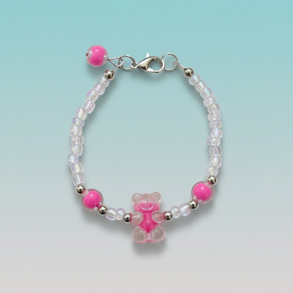 A handmade beaded charm bracelet featuring a translucent hot pink resin teddy bear charm at the center. The bracelet is crafted with alternating iridescent clear beads, small silver spacer beads, and two large accent hot pink round beads on either side. It features a silver lobster clasp closure with an adjustable chain and a single hot pink bead dangling from the end, all set against a soft, gradient mint green background.