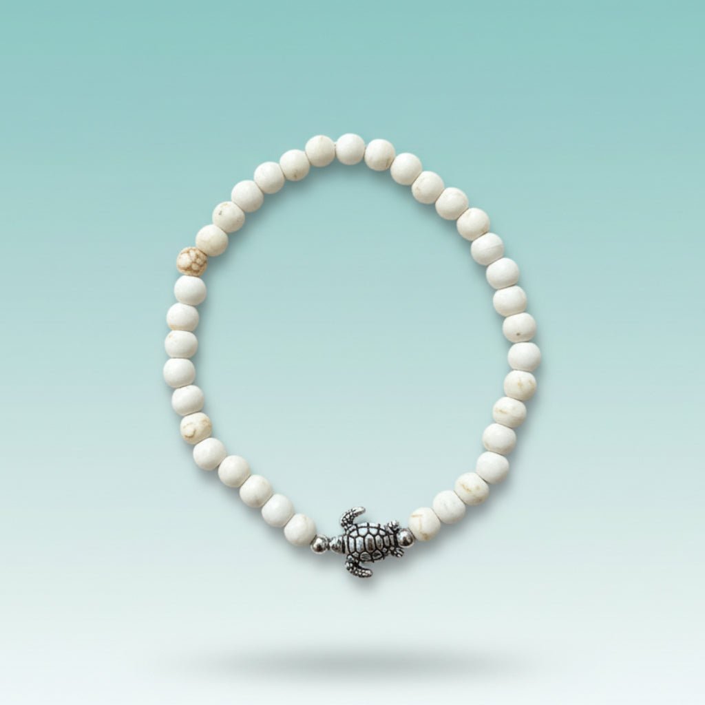 Elegant off-white beaded turtle bracelet featuring textured, marble-patterned round beads and a central silver-toned turtle charm, displayed against a soft gradient turquoise background.