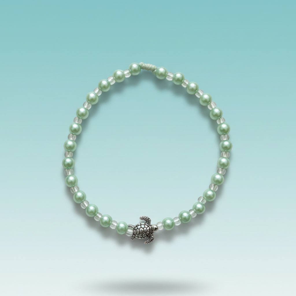 Seafoam green beaded charm bracelet featuring a polished silver turtle centerpiece, arranged in a perfect circle against a soft, gradient light-blue background.