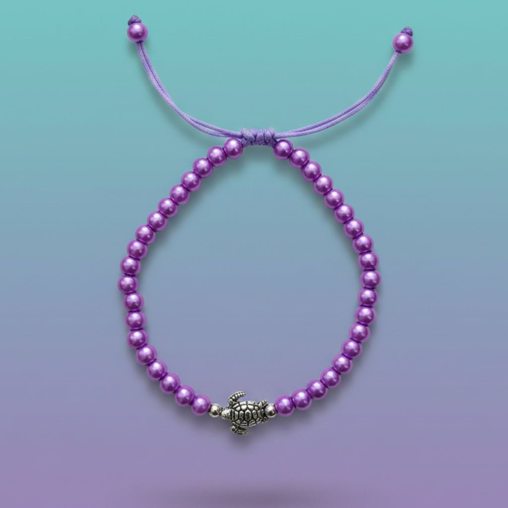 Vibrant purple beaded turtle bracelet with an adjustable pull-string cord, featuring a detailed silver turtle charm centerpiece against a soft blue and purple gradient background.