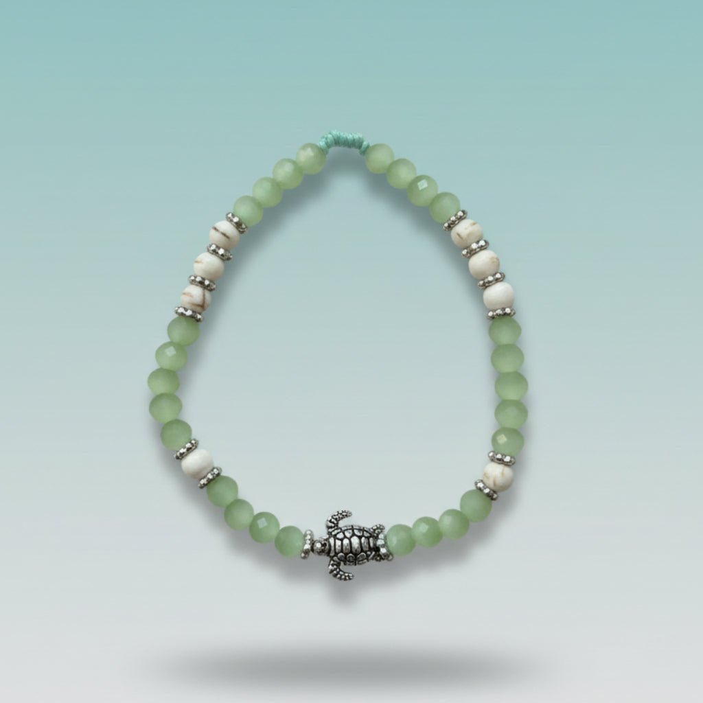 Mint green and white beaded bracelet featuring a detailed silver turtle charm centerpiece, displayed against a soft blue background.