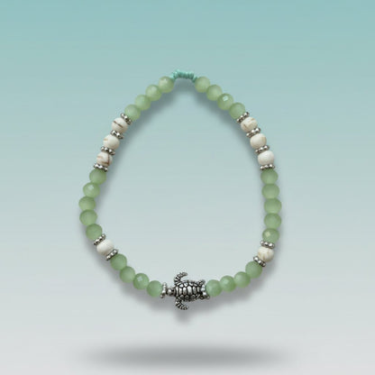 Mint green and white beaded bracelet featuring a detailed silver turtle charm centerpiece, displayed against a soft blue background.
