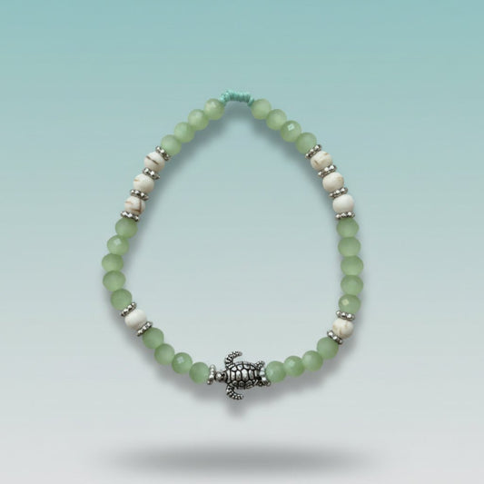 Mint green and white beaded bracelet featuring a detailed silver turtle charm centerpiece, displayed against a soft blue background.